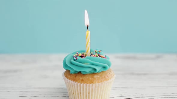 Birthday greetings concept. Blow out a candle on a muffin or cupcake. Blue background