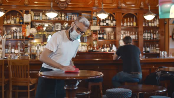 Waiter Wearing Protection Face Mask in Apron Cleaning Table with Disinfectant Spray