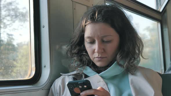 Focused Woman Rides a Train with a Phone in Her Hands and Carefully Reads the Messages on the Screen