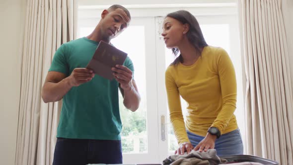 Happy biracial couple packing suitcase for travel and checking their passport