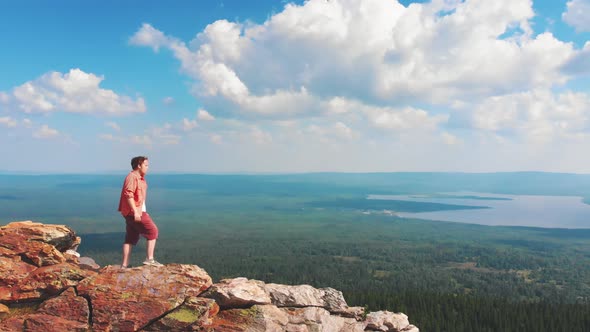 Young Man Standing on a Rocky Mountain and Putting on Sunglasses - Watching the View