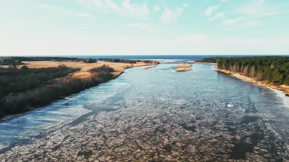 Aerial Low Flight Over Melting Snow and Ice at River Joining Sea in Spring