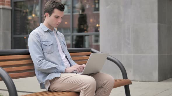 Young Man working on Laptop, Sitting on Bench