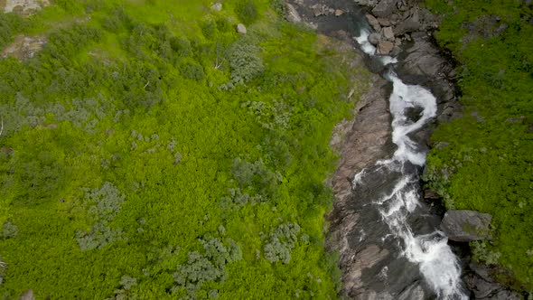 Aerial flyover idyllic Norwegian stream along green mountains in Norway