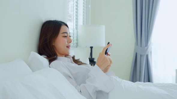 Asian attractive woman use mobile phone chat on bed at home in morning lying down and enjoy holiday.