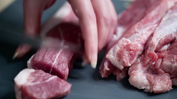 Female hands holding a knife, cut raw meat into small pieces. Close up view