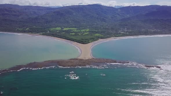 Aerial shot flying towards the whale tail shaped rocky point of Punta Uvita with green rainforest in