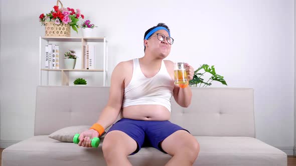 Funny fat Asian guy in sportswear lifting dumbbell weight training with enjoy drinking beer