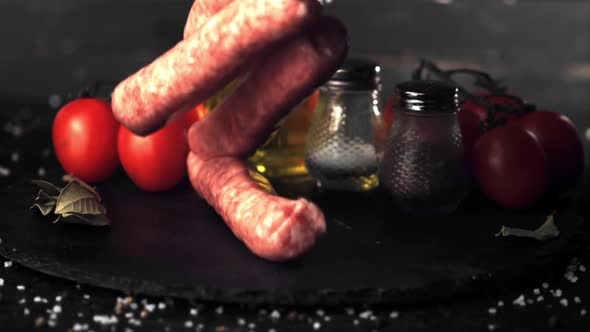 Super Slow Motion on a Stone Board with Tomatoes and Spices Falling Raw Sausages