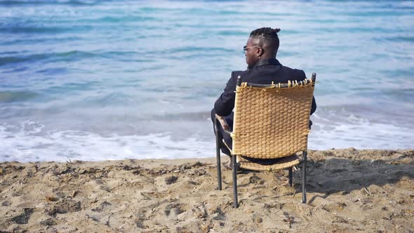 Back View Wicker Chair with African American Young Man in Formal Suit Sitting Admiring Beauty of