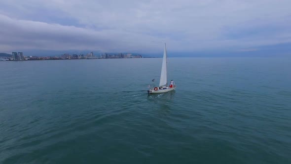 Boat Swimming Under Sails Across Sea Against Batumi, Couple Standing at Bow