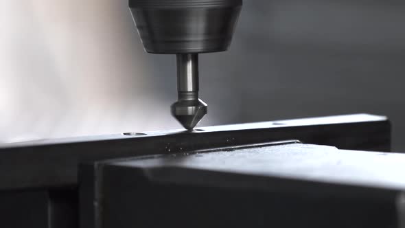 Detail steel bars being drilled by a drill press to create a structure in a machine shop.