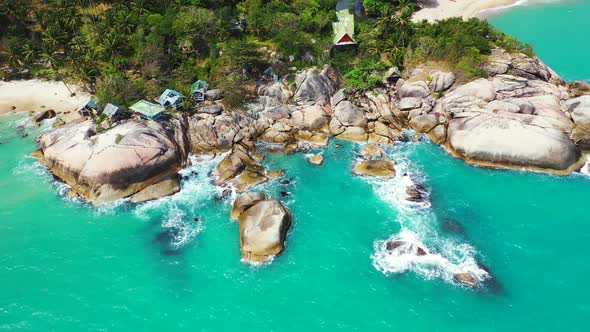 Rocky tropical shore with the houses on the waterfront. Turquoise lagoon and foamy waves washing on