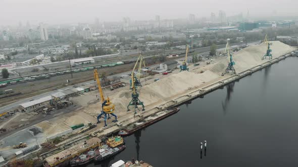 Aerial view of cargo port cranes near a pile of sand with ships, scows and barges