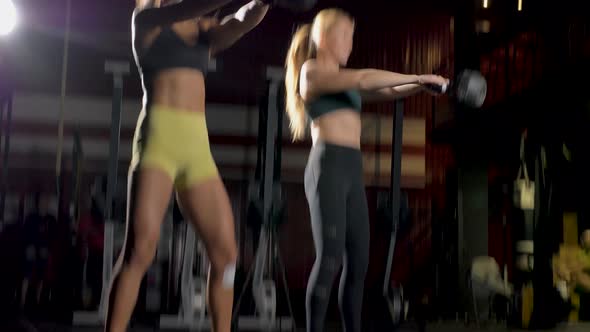 Two Strong Athletic Women Simultaneously Lift Kettlebells in the Gym