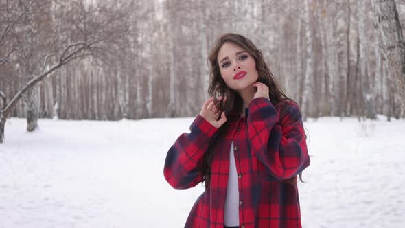 Young Woman with Wavy Hair Standing and Touching Face in Winter Forest