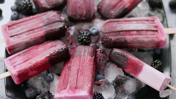 Homemade Fresh Frozen Blueberry and Blackberry Popsicles on Black Plate with Ice Sitting on Stone