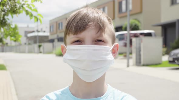 A Young Boy Puts on a Face Mask, Looks at the Camera, Takes the Mask Off in an Empty Suburban Area