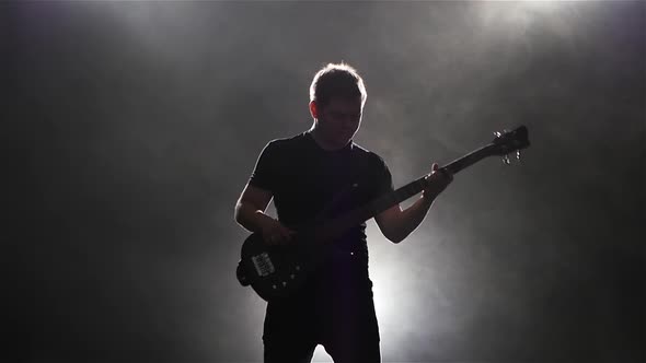 Dark Background with Smoke. Playing Man on Black Bass Guitar