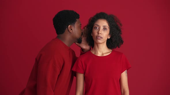 Handsome African man talking secret to his shocked girlfriend