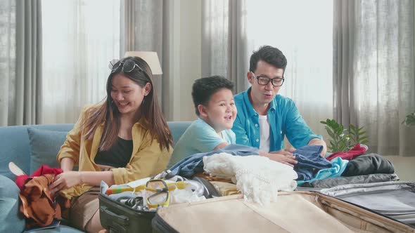 Happy Asian Family Packing Clothes In A Suitcase For A New Journey. Luggage For Travel Holidays