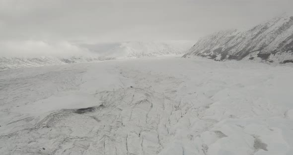 Aerial helicopter shot, tilt up from craggy glacier to see mountains and Alaskan wilderness, high mo