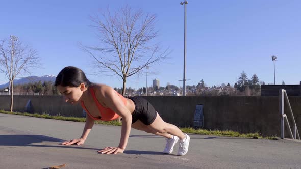 Athletic young woman doing pushups outdoors. Wide shot