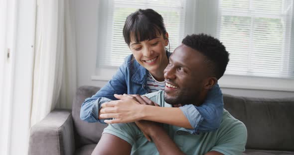 Portrait of happy diverse couple sitting on couch and embracing in living room