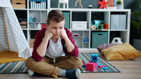 Slow Motion of Lonely Child Sitting on Floor in Playroom Feeling Miserable and Bored