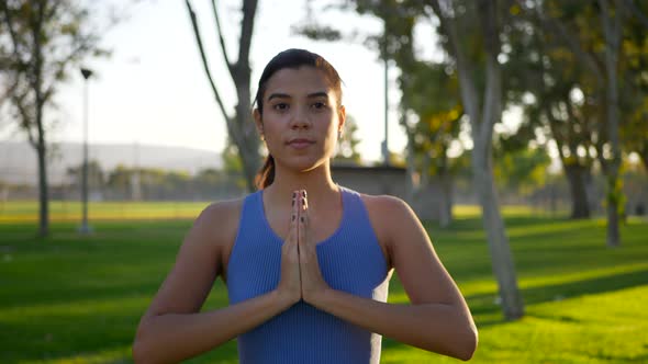 A pretty woman in a prayer hands yoga pose meditating in the park at sunrise.