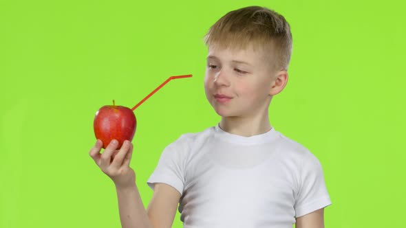 Little Boy Is Holding an Apple with a Straw, Showing Thumbs Up. Green Screen