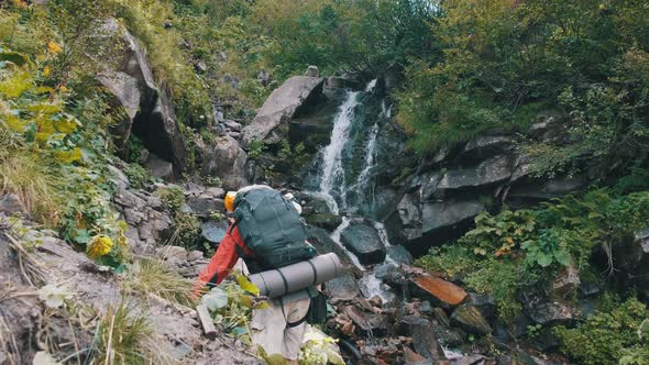 Tourist with Backpack Came To Mountain Waterfall and Spreading Arms To Sides