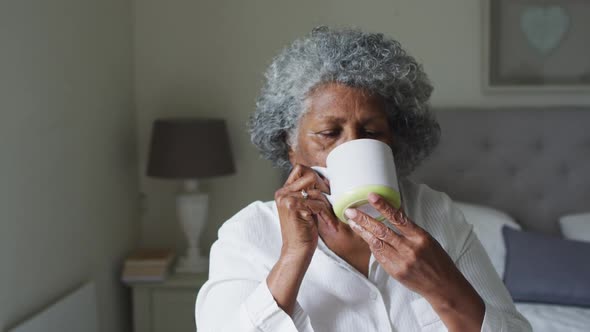 Senior african american woman drinking coffee while sitting on the bed at home