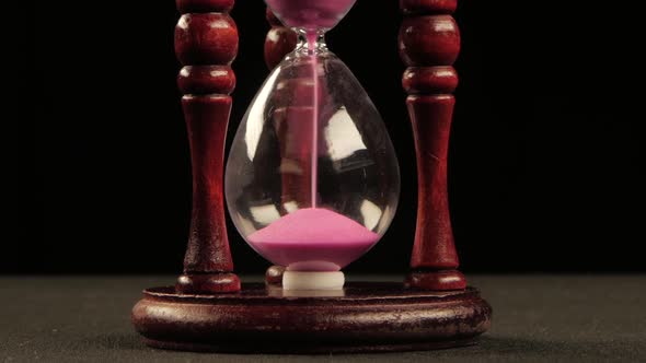 Hourglass in Wooden Stand. Pink Sand. Black. Close Up