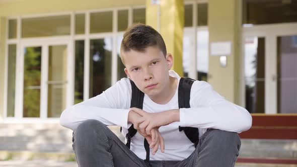 A Caucasian Teenage Boy Looks Seriously at the Camera As He Sits in Front of School  Closeup