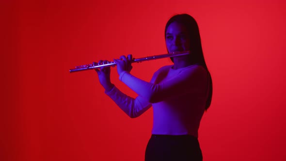 Smooth flute playing on colored background. Girl in a white blouse plays wind instrument flute