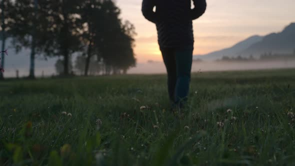 Man Walking Through Meadow Towards Foggy Landscape And Sunrise