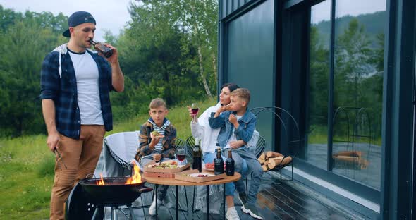 Father and His Wife Drinking Wine and Children Eating Pieces of Pizza Around the Table Outdoors