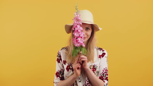 White Woman with Long Blonde Hair Wearing Sun Hat Playfully Covering Face with Pink Delphinium