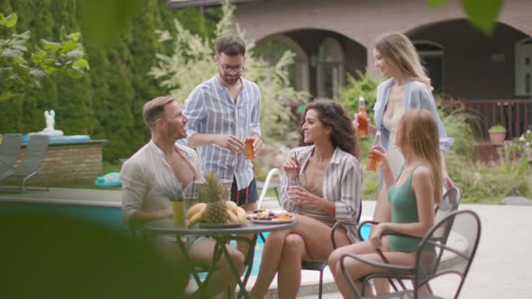 Group of happy young people cheering with cider by the pool in the garden