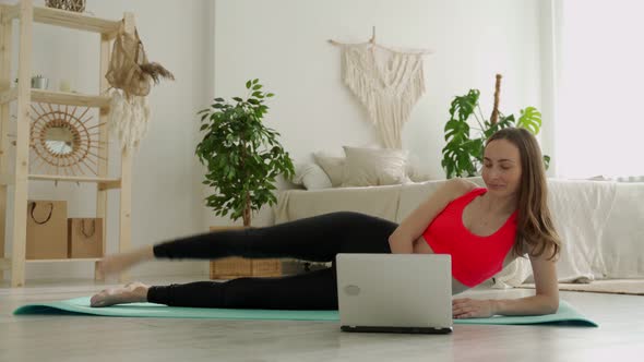 Leg Raise From Lying Position of a Young Woman She is Doing Her Exercises at Home Using a Laptop