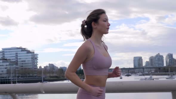 Asian Woman jogs across bridge in Downtown Vancouver BC landscape, Slowmo