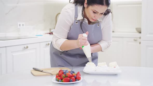 a Female Chef Adds Cream From a Pastry Bag to Anna Pavlova Cakes in the Kitchen