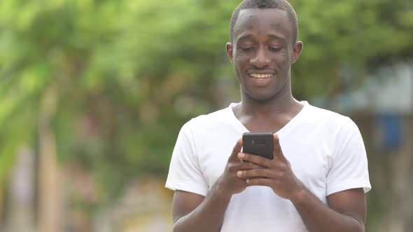 Young Happy African Man Smiling While Using Phone in the Streets Outdoors