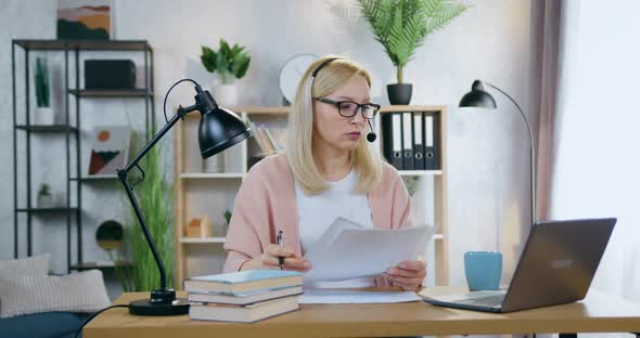 Businesswoman in Headset Sitting in front of Laptop in Cozy Home Office During Video Meeting