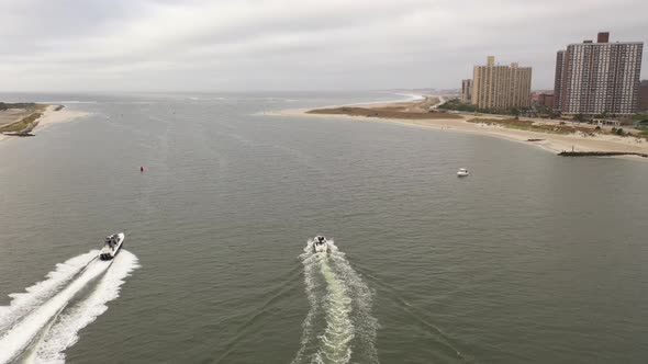 An aerial view over East Rockaway Inlet as two boats speed by leaving a white wake behind. The camer