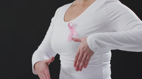 Mid section of a woman showing the pink ribbon on her chest against black background