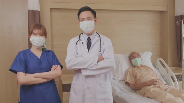 Portrait of Asian doctor and nurse standing and crossing arms in the recovery room of eldery patient