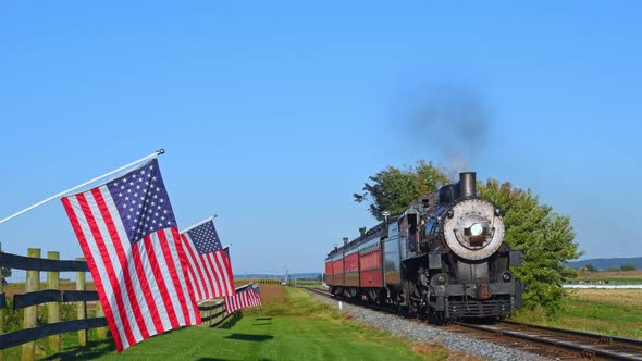 View of a Line of Gently Waving American Flags on a Fence by Farmlands as a Steam Passenger Train Bl