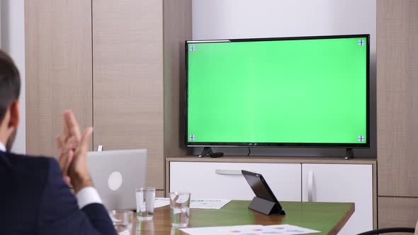 Businessman in Conference Room Talking with a Green Screen TV